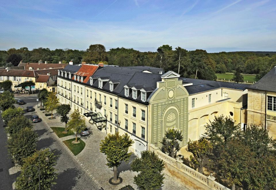 a large building with a clock tower is surrounded by trees and cars on the street at Auberge du Jeu de Paume