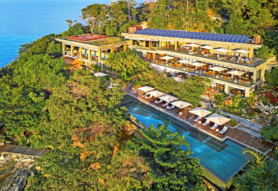 a resort with a large pool surrounded by lounge chairs and umbrellas , as well as trees in the background at Six Senses Krabey Island