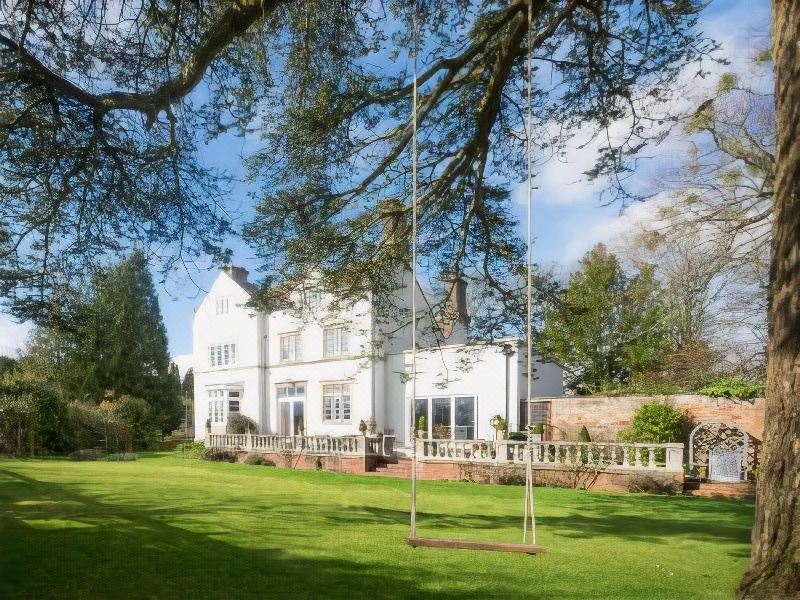 a white house with a swing hanging from a tree in the backyard , surrounded by green grass and trees at Blaisdon House B&B