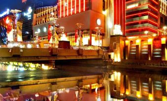 a nighttime scene of a hotel with red and blue lights reflecting in a body of water at Novotel Jakarta Mangga Dua Square