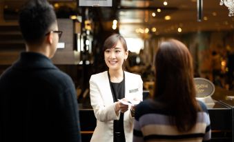 A woman is standing in front of an audience at a table, while another person is sitting down at Panda Hotel