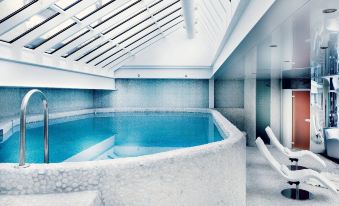 an indoor swimming pool with blue water , surrounded by white walls and a skylight above at Hotel Mont Blanc Megève