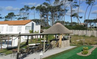 a courtyard with a thatched roof gazebo surrounded by grass , chairs , and tables in the background at Punta del Este Arenas Hotel