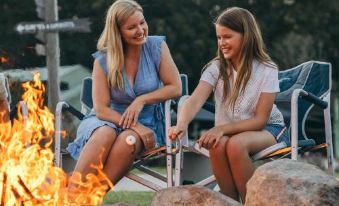 a woman and a young girl are sitting next to a campfire , toasting marshmallows over them at Paradise Country Farmstay