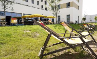 a group of lounge chairs are placed in a grassy area next to a building at Hey Lou Hotel Frankfurt Airport