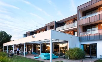 a modern building with a white exterior , surrounded by green grass and blue chairs under a covered area at Best Western Plus Hotel les Rives du Ter