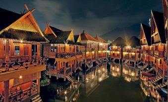 a picturesque scene of a small wooden village at night , surrounded by water and illuminated by lights at Danau Dariza Resort  - Hotel