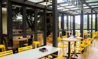 a modern restaurant with yellow chairs and tables , surrounded by large windows and a glass ceiling at Marbella Twin Waterfall Resort Ciater