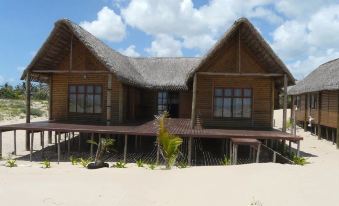 a wooden house with a thatched roof is surrounded by a sandy beach and palm trees at White Sands