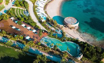 an aerial view of a resort with a pool surrounded by lounge chairs , umbrellas , and palm trees at Le Méridien Bodrum Beach Resort