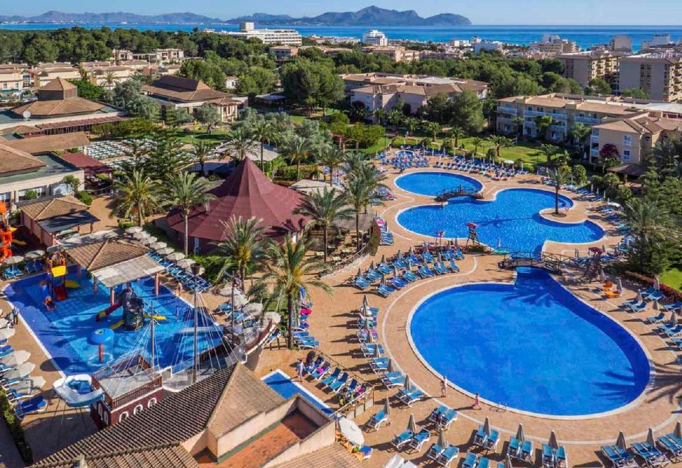 an aerial view of a resort with a large pool surrounded by multiple buildings and a beach in the background at Zafiro Can Picafort