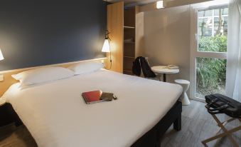 a large bed with a book on it is in a room with a window and chair at Ibis Nantes Saint-Herblain