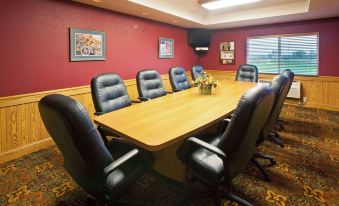 a conference room with a large wooden table surrounded by black leather chairs , and a television mounted on the wall at AmericInn by Wyndham Anamosa