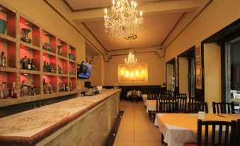 a modern restaurant interior with white walls , wooden floors , and a large chandelier , featuring a bar counter and several tables set for dining at Hotel Luna