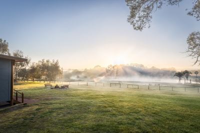 a man is sitting on a bench in a grassy field , enjoying the sunrise over a misty lake at The Swan Valley Retreat
