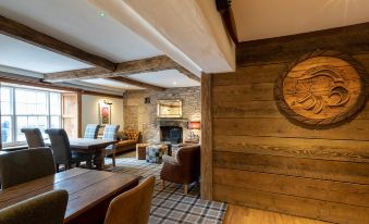 a rustic dining room with wooden furniture , including a dining table , chairs , and a fireplace at The Greyhound Hotel