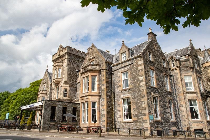 a large , old stone building with multiple windows and doors , situated on a street in a town at The Tarbet Hotel