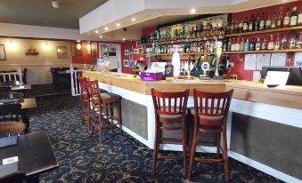 a bar with a wooden counter and chairs , surrounded by bottles of liquor on the counter at The George Hotel