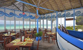 a restaurant with blue and white walls , wooden tables , chairs , and a view of the ocean at Tryp Cayo Coco