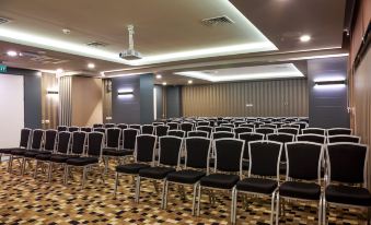 an empty conference room with rows of black chairs and a white ceiling , ready for a meeting or event at Sunprime C-Lounge