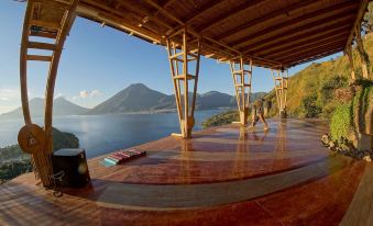 a woman sitting on a yoga mat in a hot tub , surrounded by mountains and a lake at Eagle's Retreats