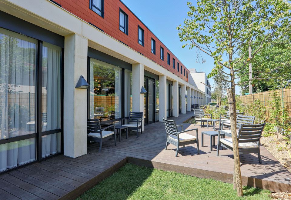 a row of outdoor dining areas with tables and chairs , located next to a building at Hampton by Hilton Toulouse Airport
