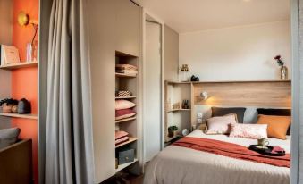 a bedroom with a bed , nightstand , and shelves is shown with a curtain covering the window at Camping le Parc de Paris