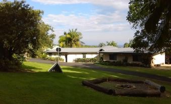 a large white building with a sloping roof , surrounded by trees and grass , under a blue sky with clouds at Alstonville Country Cottages