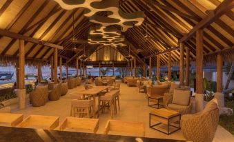 a large , open - air restaurant with wooden furniture and a thatched roof , providing a comfortable and inviting atmosphere at Fushifaru Maldives