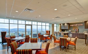 a modern hotel lobby with large windows , wooden tables and chairs , and multiple seating options at Home2 Suites by Hilton Dickson City Scranton
