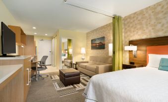 a modern hotel room with a comfortable bed , couch , and desk , as well as a living area with a chair and table at Home2 Suites by Hilton Baton Rouge
