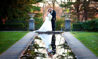 a newlywed couple is standing in a garden , with the bride 's dress and the groom 's suit at The Castle at Skylands Manor