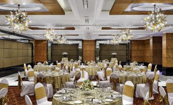 a large banquet hall with multiple tables set for a formal event , featuring white chairs and gold tablecloths at Taj Club House