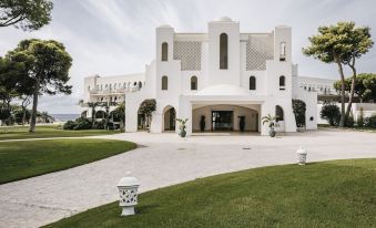 a large white building surrounded by a grassy area , with a path leading up to it at Falkensteiner Resort Capo Boi