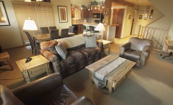 a cozy living room with a brown leather couch , two chairs , a coffee table , and a dining table at Whispering Pines