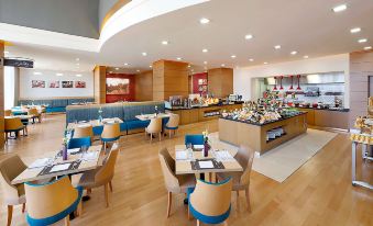 a modern cafeteria with wooden floors , blue chairs , and a dining area filled with food at Hilton Garden Inn Tabuk