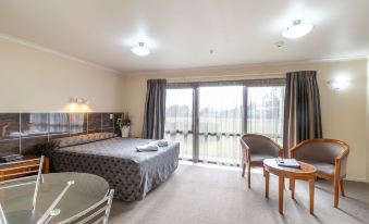 a hotel room with a large bed , a desk , a chair , and a window overlooking a golf course at Admirals Motor Inn