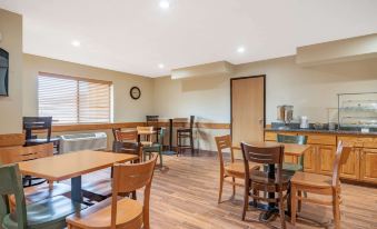 a dining area with wooden tables and chairs , as well as a kitchen in the background at AmericInn by Wyndham Rogers