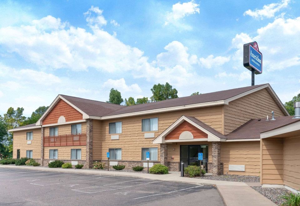 a building with a brown roof and brown siding is surrounded by a parking lot at AmericInn by Wyndham Rogers