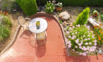 a small , red brick patio with a table and chairs surrounded by potted plants and flowers at Lona