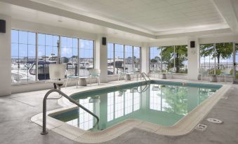 a large indoor swimming pool with a glass wall , surrounded by lounge chairs and umbrellas , in a sunny outdoor setting at Hilton Garden Inn Kent Island