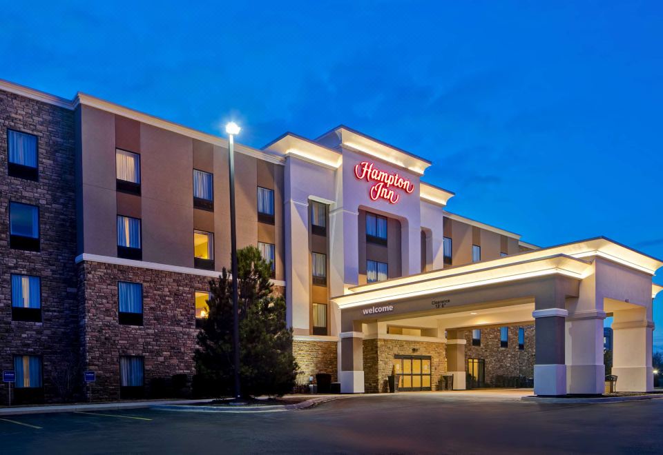 an exterior view of a hampton inn hotel , with a large parking lot visible in the foreground at Hampton Inn-DeKalb (Near the University)