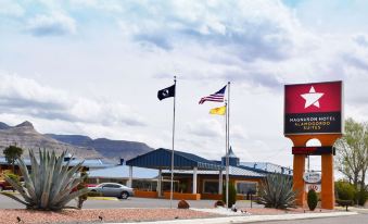 a red car is parked in front of a hotel with american and texas flags flying at The Classic Desert Aire Hotel