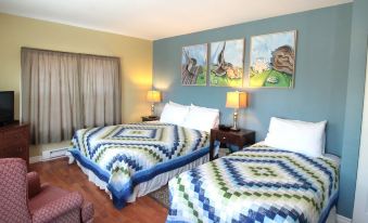 a hotel room with two beds , each made up with colorful quilts and pillows , along with curtains and artwork on the walls at Seawind Landing Country Inn