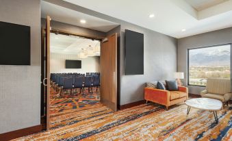 a spacious conference room with a couch , chairs , and a large screen mounted on the wall at Embassy Suites by Hilton South Jordan Salt Lake City