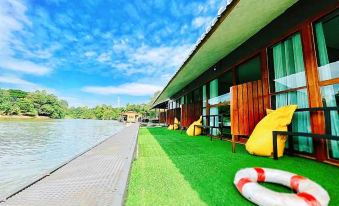 a modern building with a green roof and yellow walls , surrounded by a moat and blue sky at Baanrai Riverkkwai Resort