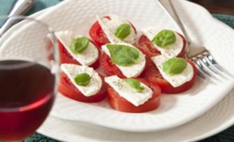 a white plate with slices of tomato and mozzarella cheese on it , accompanied by a glass of wine at The Waterford Inne