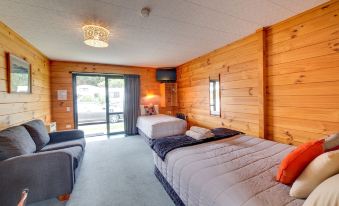 a cozy hotel room with wooden walls , two beds , and a balcony , decorated with blue curtains and orange pillows at Wellington Top 10 Holiday Park