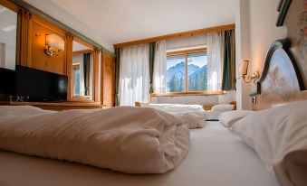 a hotel room with two beds , one on each side of the room , and a tv mounted on the wall at Hotel Dolomiti Schloss