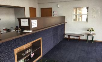 a reception area with a blue carpet , a desk , and a wooden counter with a vase of flowers at Thunderbird Motel Hillsboro